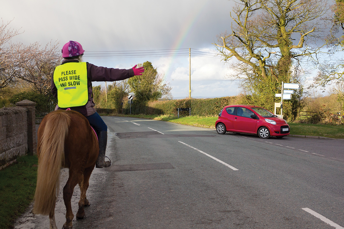 An equestrian wearing bright colors for safety while riding her horse on a road